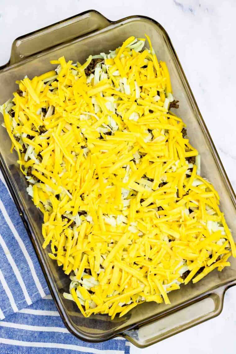 Shredded cheese on top of beef and onions in a baking dish