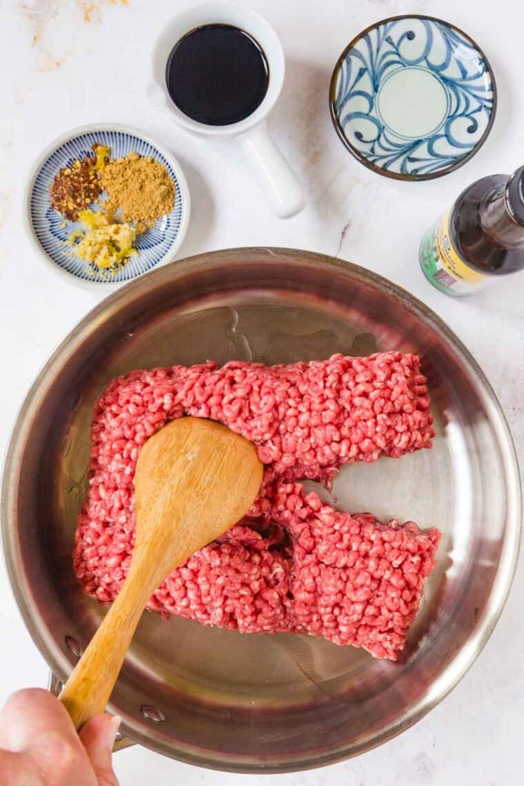 Ground beef in a pot, being broken up with a wooden spoon.