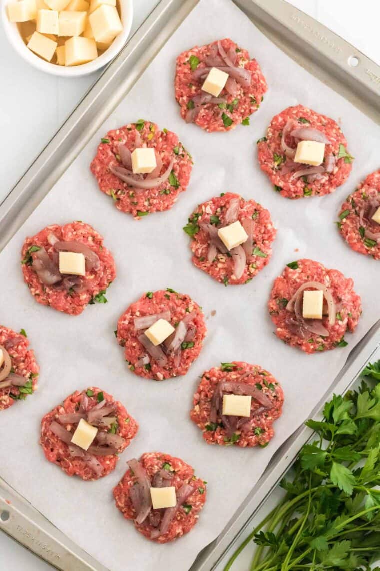 Onions and cheese placed in the centers of meatball patties on a baking tray..