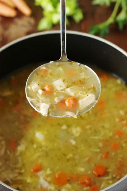 A ladle of chicken soup over a pot.