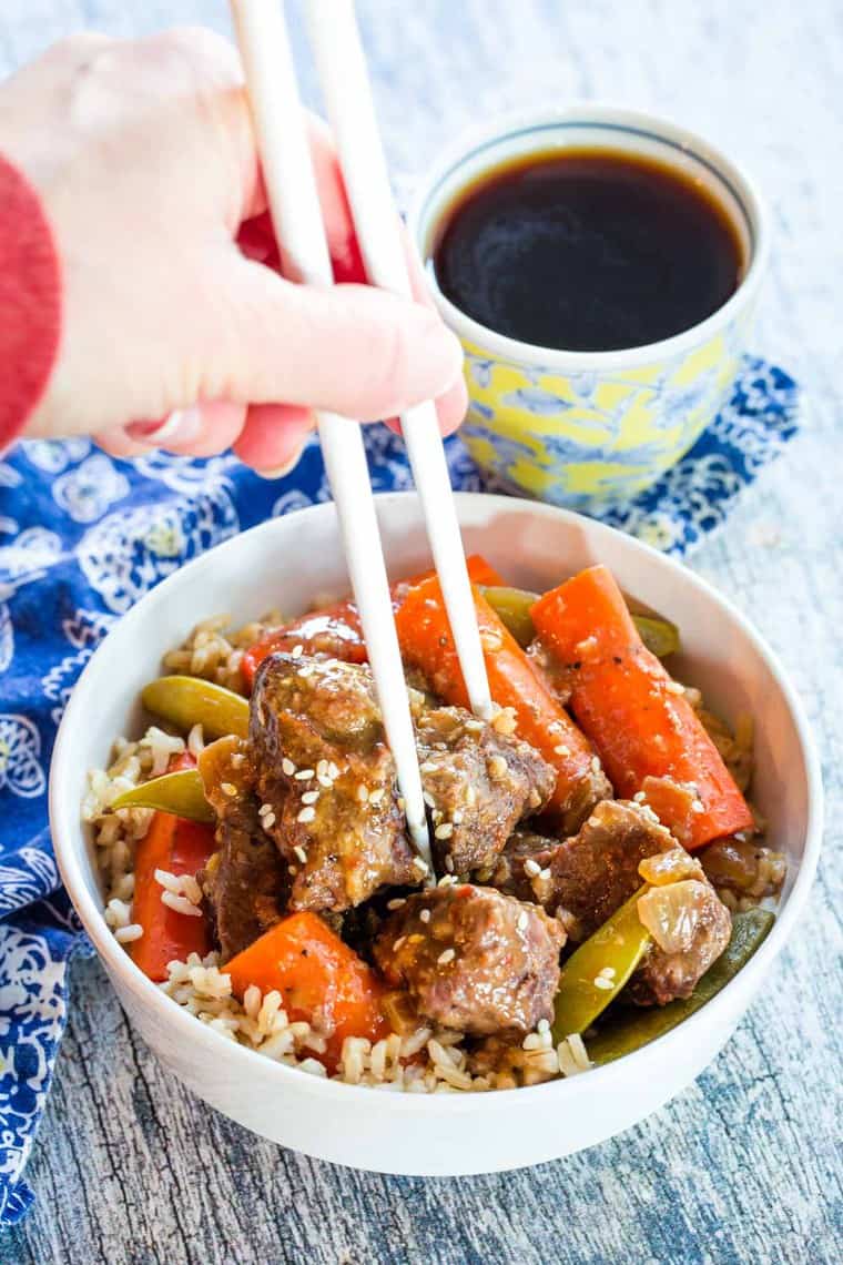 Using chopsticks to eat Slow Cooker Mongolian Beef Stew with rice in a white bowl