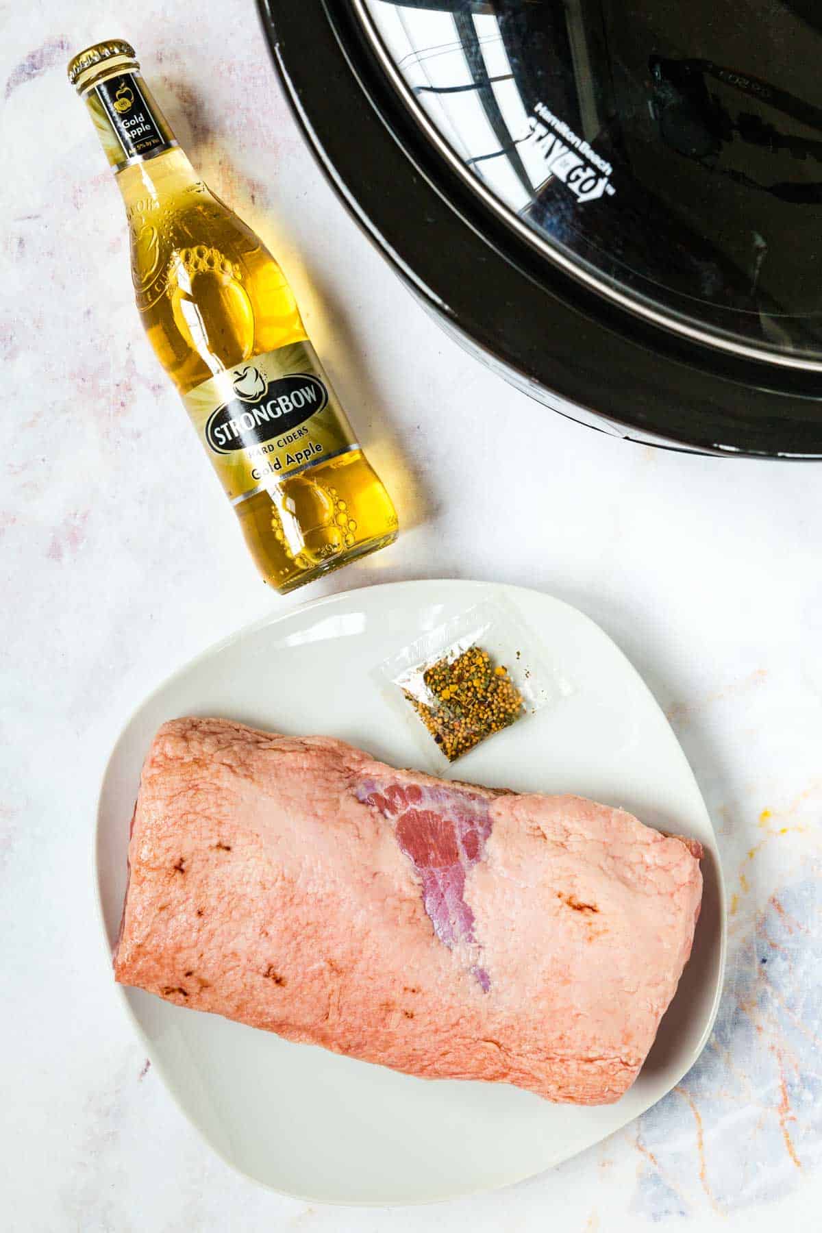 The ingredients for slow cooker corned beef: Beef brisket and hard cider next to a Crock Pot.