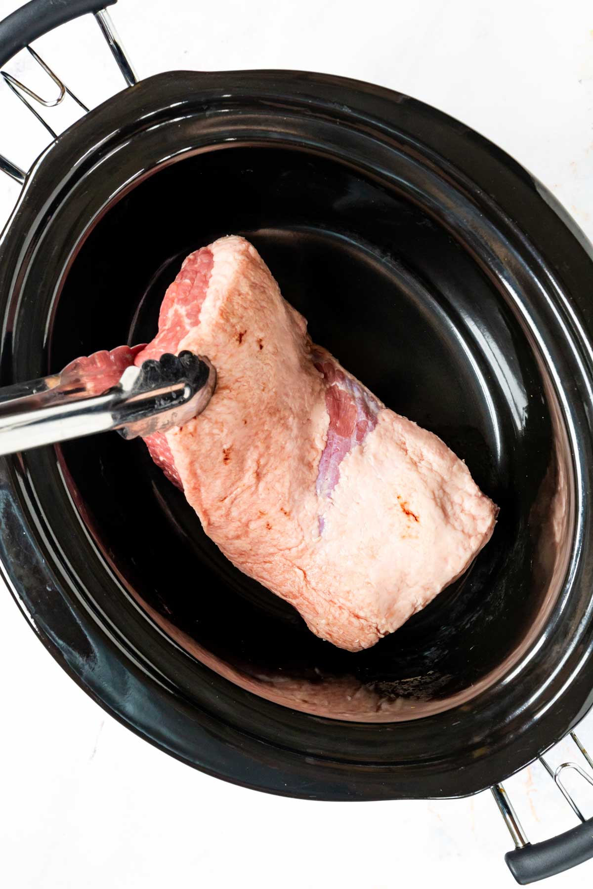 A cut of brisket is placed into the bowl of a slow cooker.