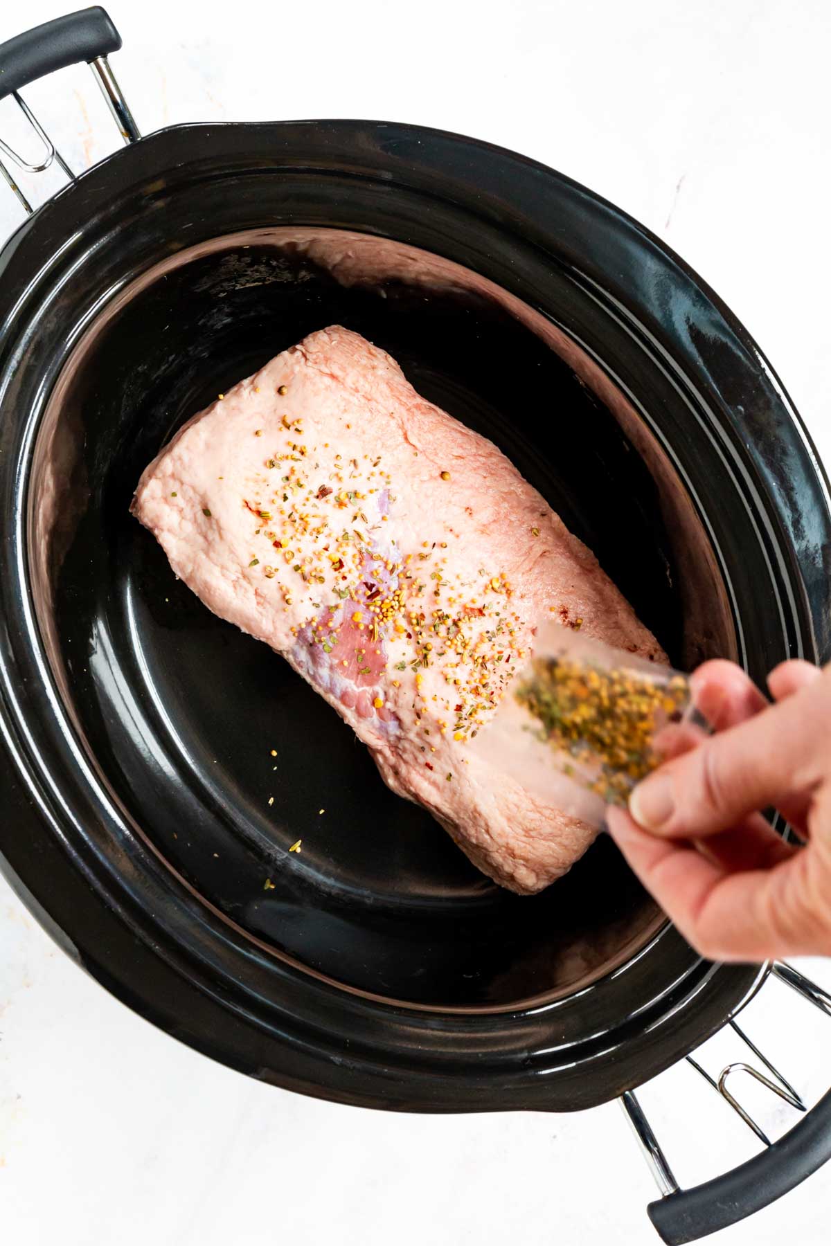 The brisket seasoning is sprinkled into the slow cooker overtop the cut of corned brisket.