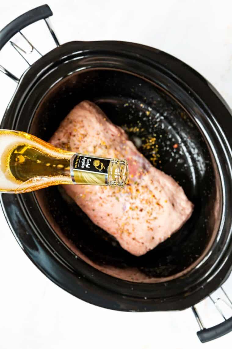 Hard cider being poured over the seasoned beef brisket in a slow cooker.