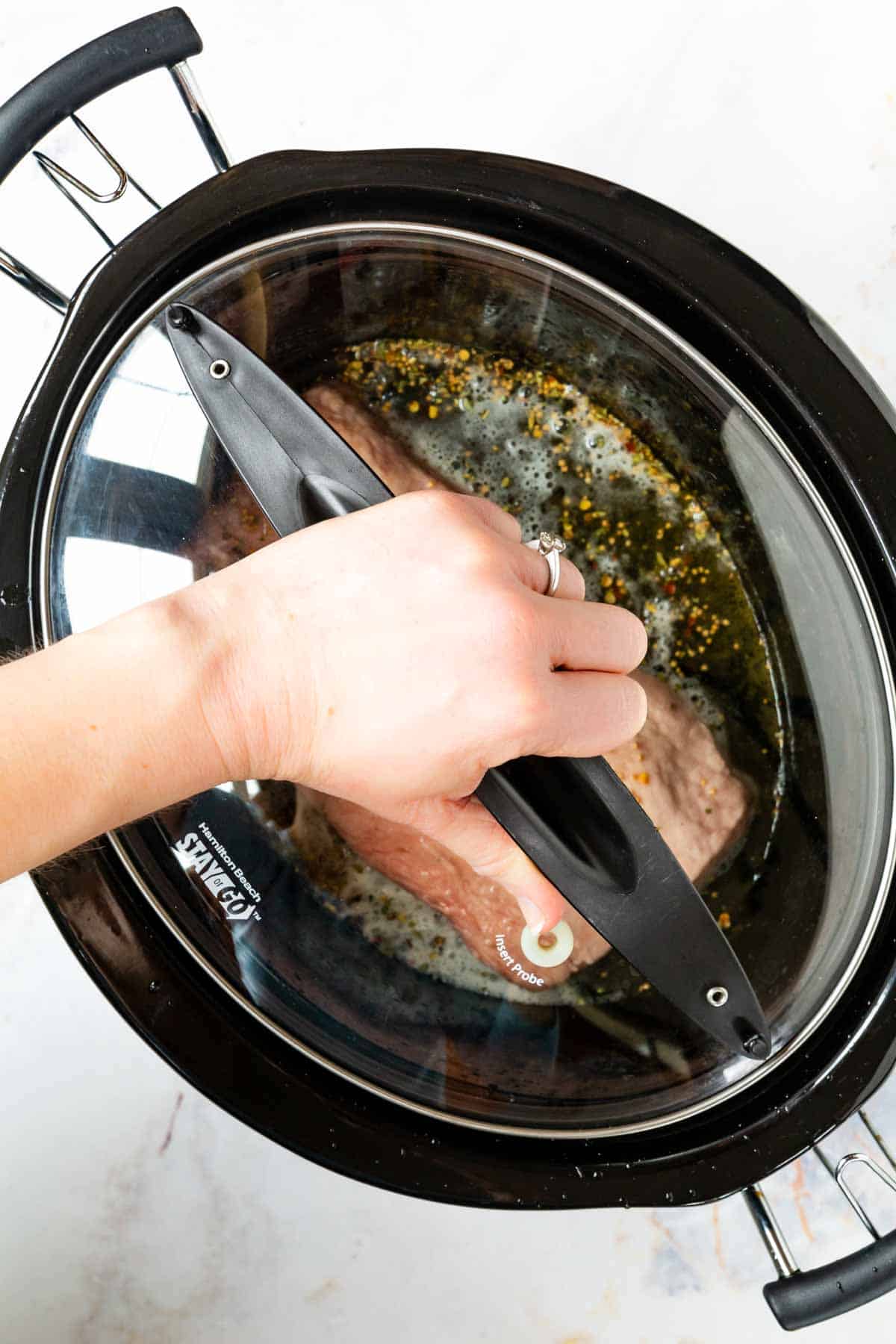 The lid being placed over a slow cooker filled with corned beef brisket and hard cider.