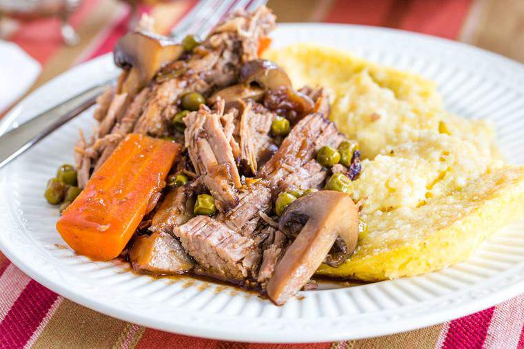 A plate of crockpot balsamic beef pot roast with mushrooms, carrots and peas over polenta