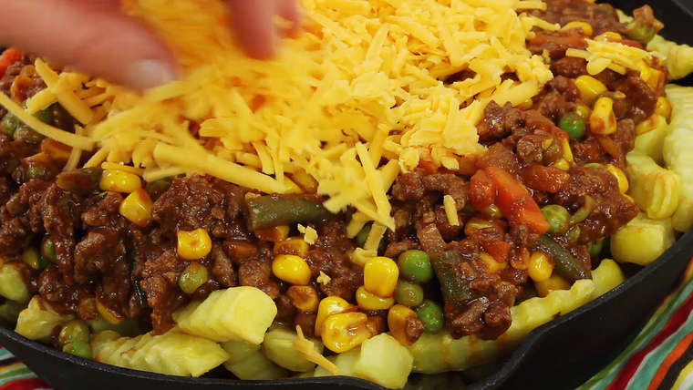 Process shot of topping Shepherd's Pie Loaded French Fries with shredded cheese