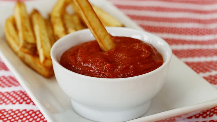 Dipping a french fry in a bowl of ketchup.