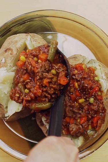 Ground beef and vegetable mixture being spooned into baked potatoes.