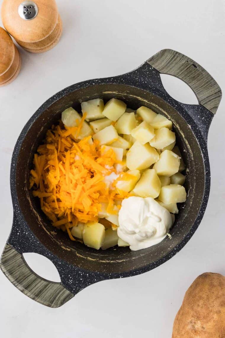 Cheddar cheese, milk, and sour cream added to boiled potatoes in a pot