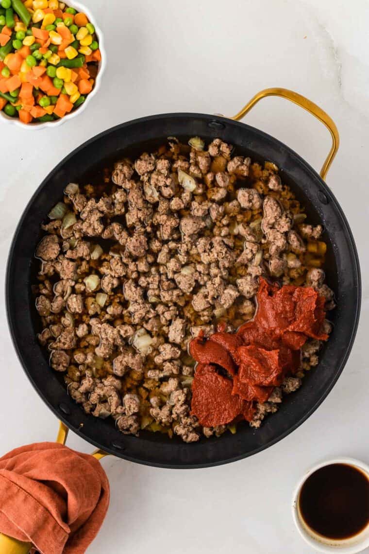 Tomato paste added to ground beef in a skillet