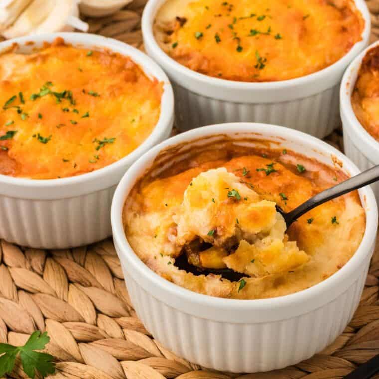 Four ramekins of mini shepherd's pies with a spoon in one