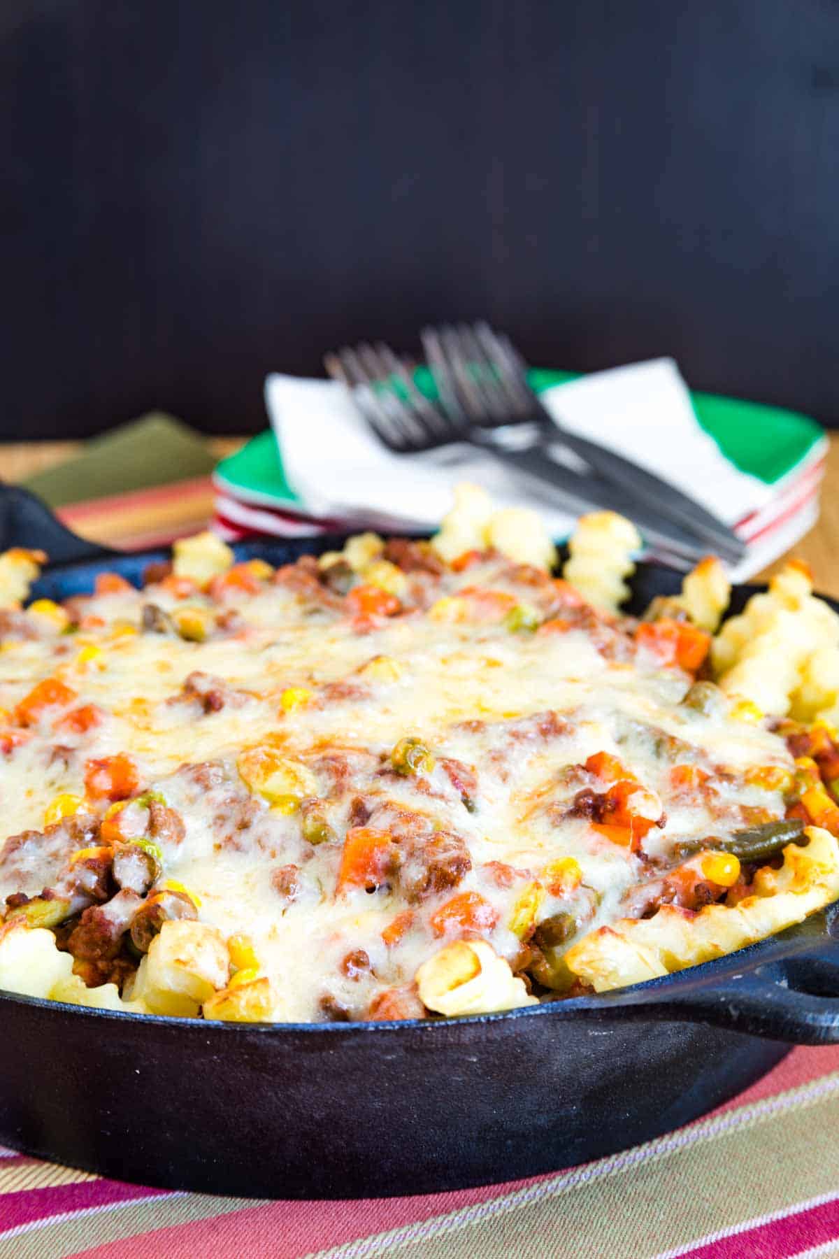 Shepherd's Pie Loaded French Fries in a cast iron skillet with a stack of plates and forks in the background.