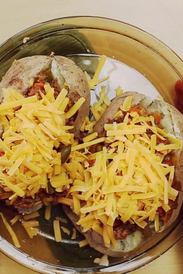 Two stuffed baked potatoes topped with shredded cheese in a round baking dish.