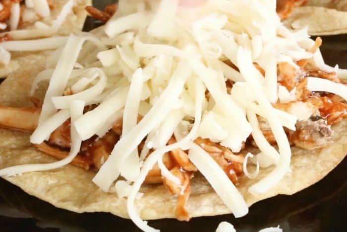 Add shredded cheese on top of barbecue chicken tostadas