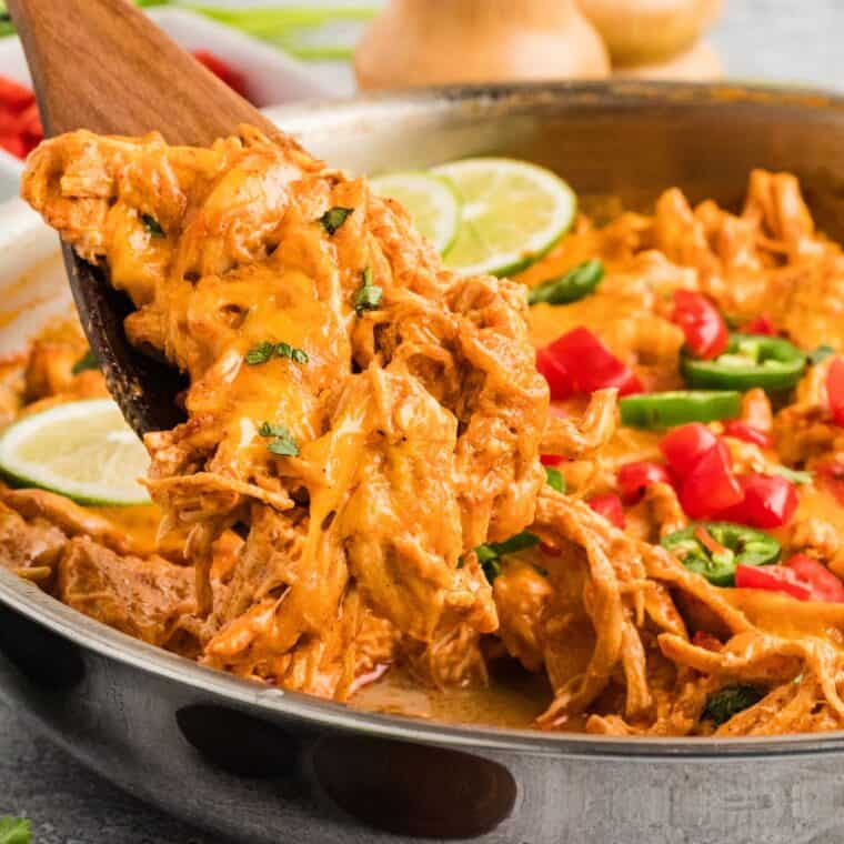A wooden spoon serving chicken enchilada skillet