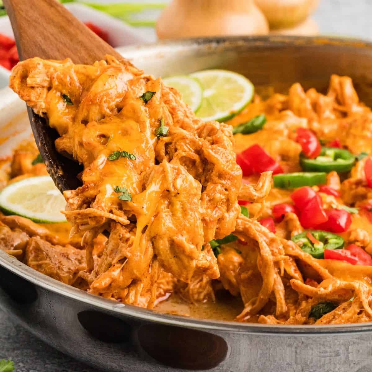 A wooden spoon serving chicken enchilada skillet