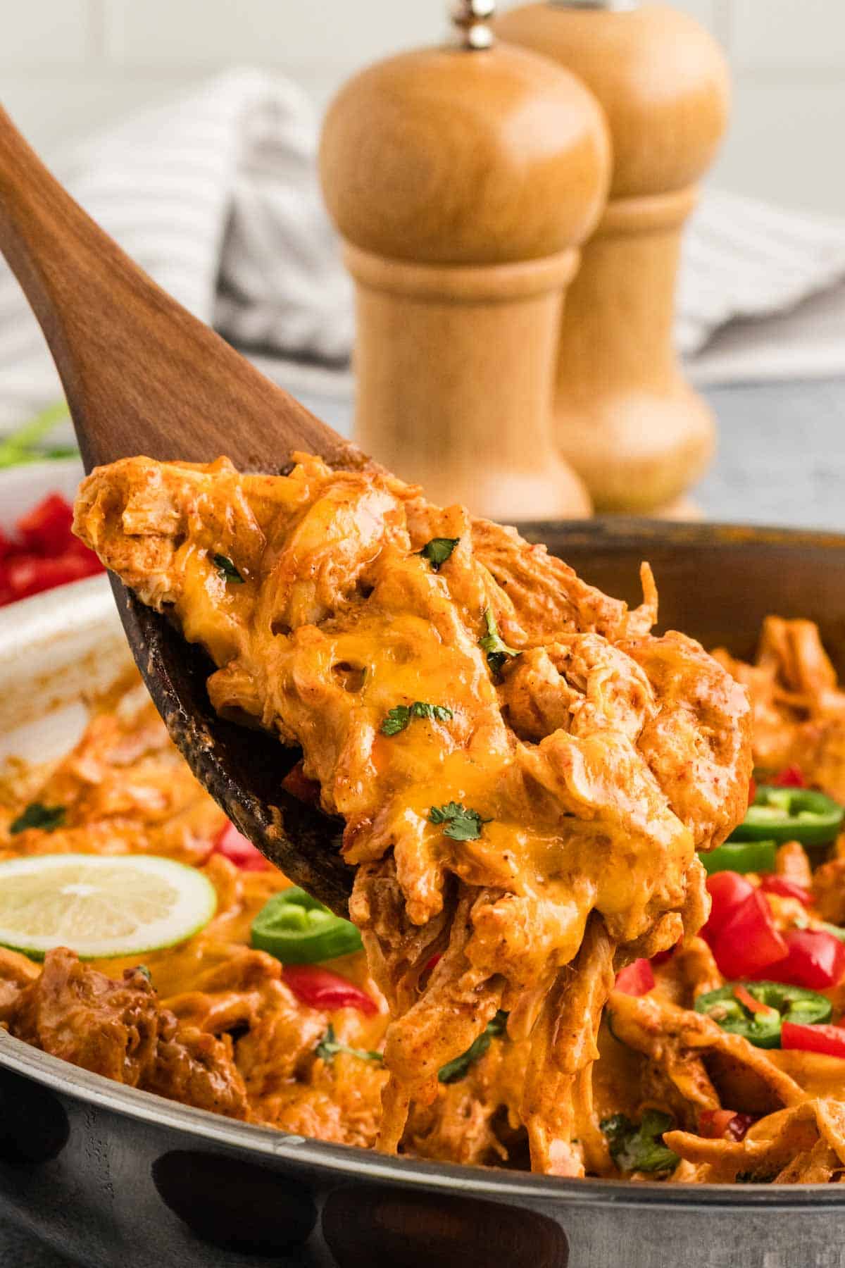 A wooden spoon serving chicken enchilada skillet 