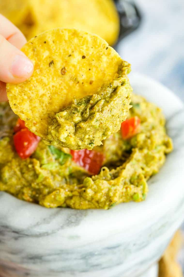 Kid friendly guacamole on a chip held by kids fingers