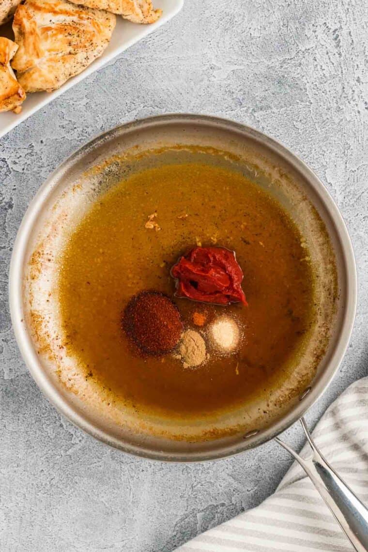 Tomato paste and seasonings added to broth in a skillet