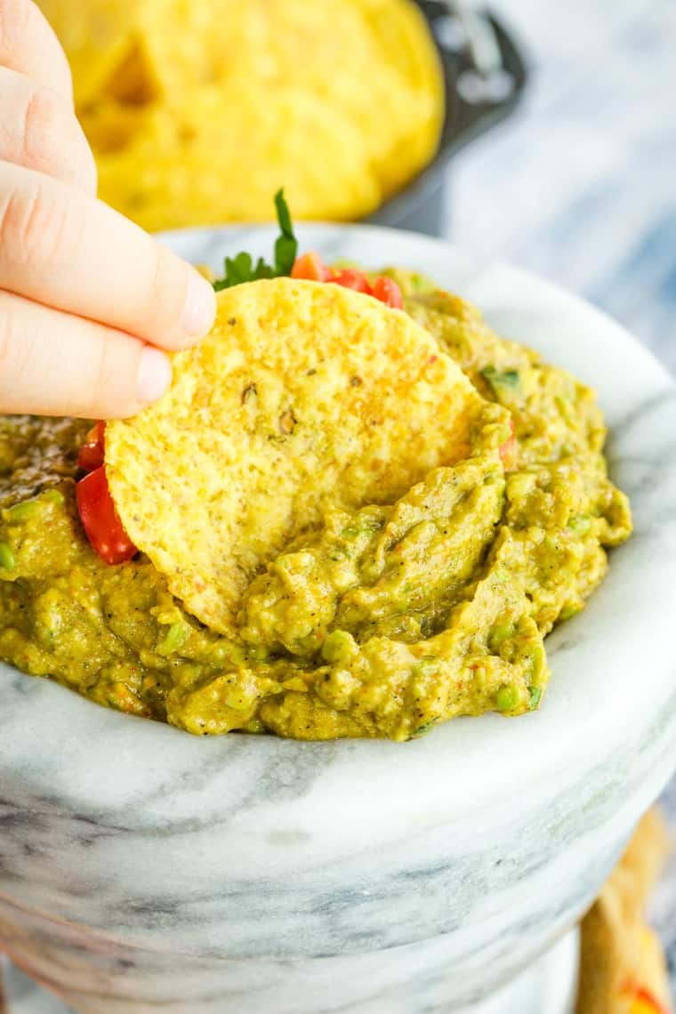 Kids fingers holding a chip to scoop guacamole