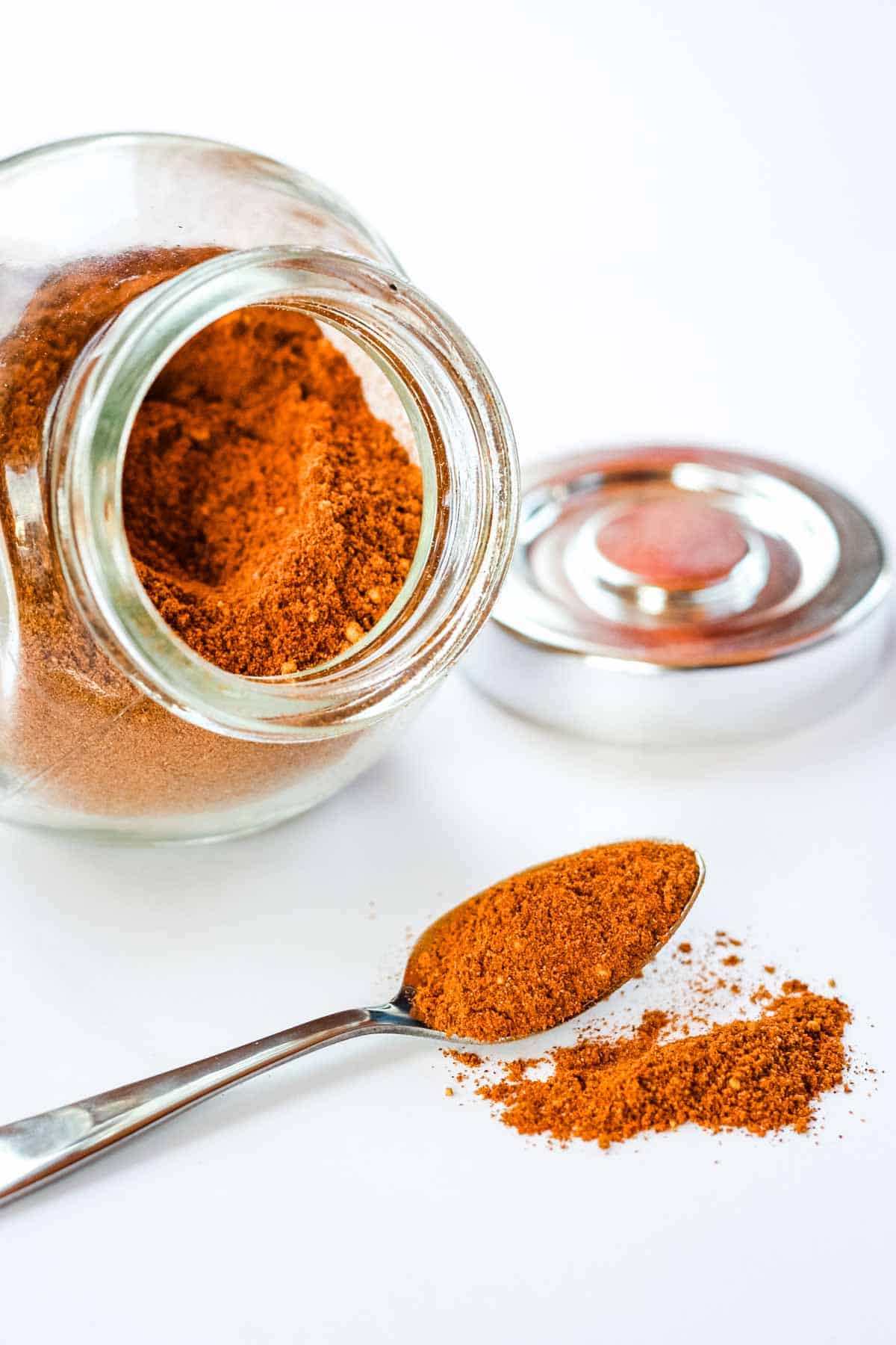 A jar and a spoon filled with a light-brown colored spice mix.