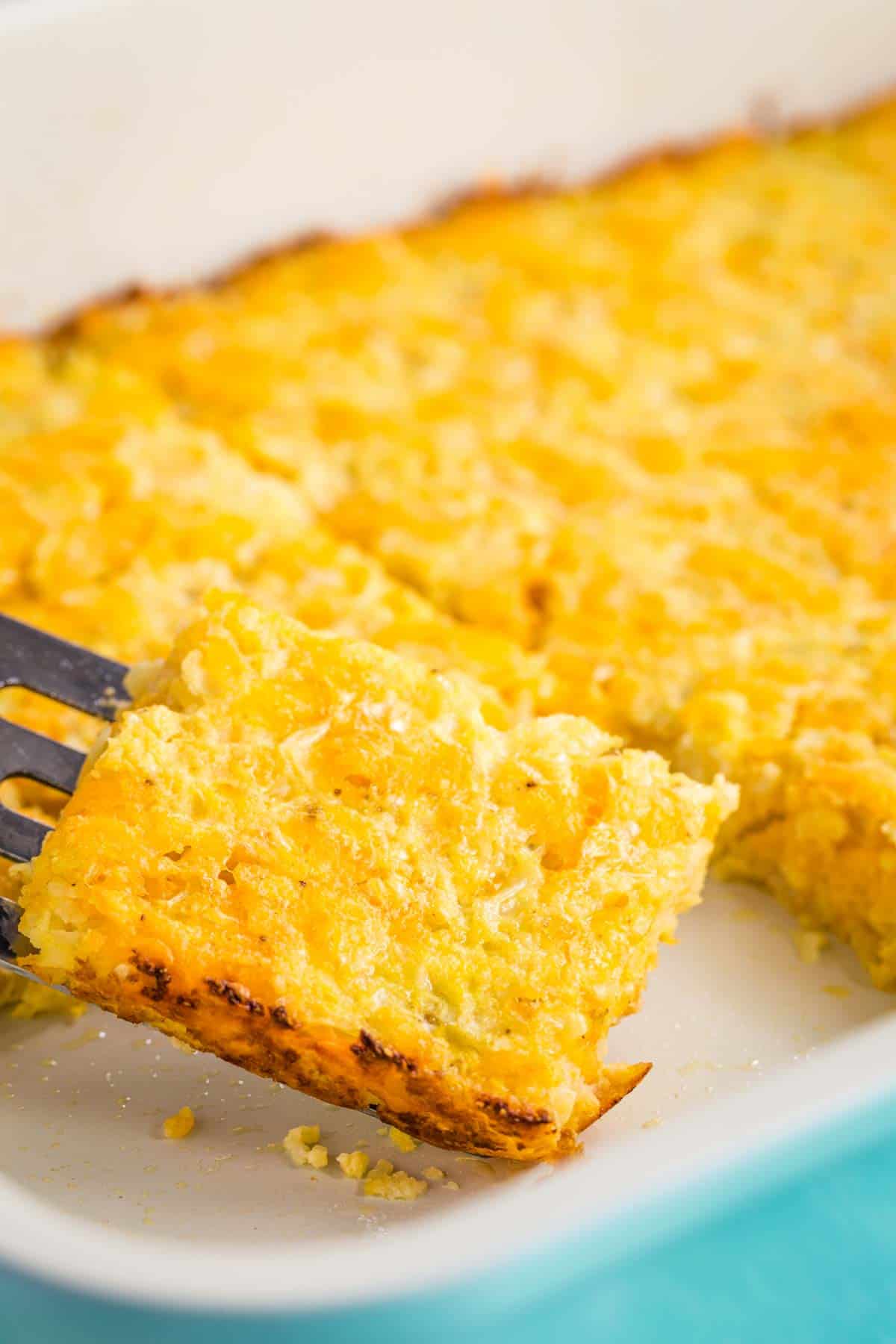 A piece of Cauliflower Hash Brown Casserole being picked up on a spatula from the baking pan.