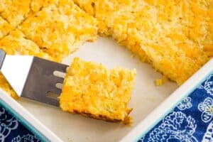 A piece of Cheesy Cauliflower hash Browns Casserole on a spatula in a baking dish