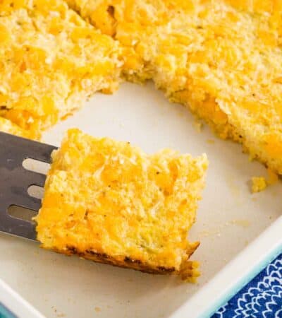A piece of Cheesy Cauliflower hash Browns Casserole on a spatula in a baking dish