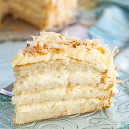 Piece of gluten free coconut cake from the side to see layers of cake, filling, and coconut buttercream frosting