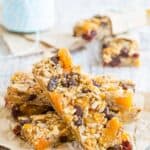 Trail Mix Gluten Free Granola Bars piled in a criss-crossed manner on a square of parchment paper.