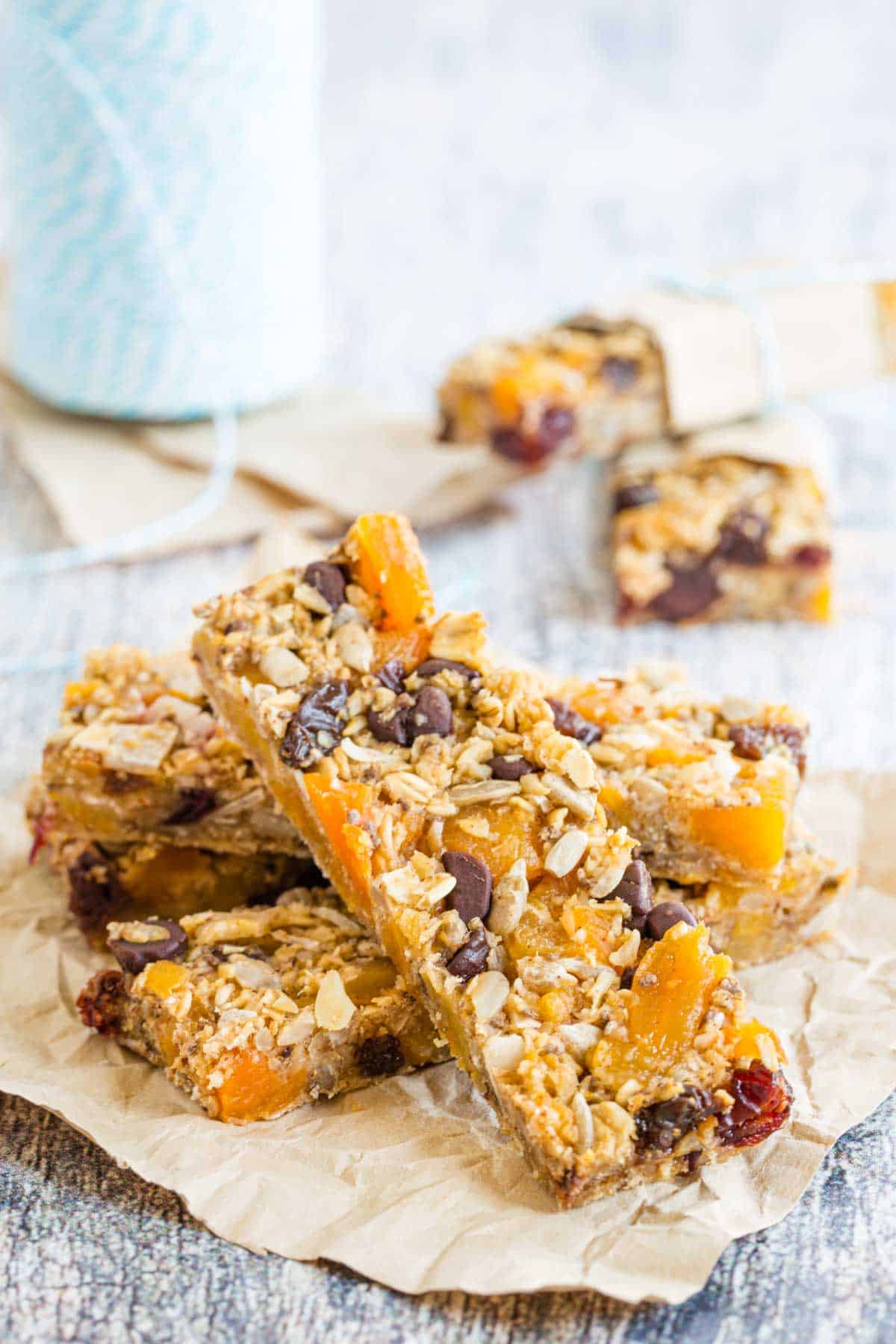 Trail Mix Gluten Free Granola Bars piled in a criss-crossed manner on a square of parchment paper.
