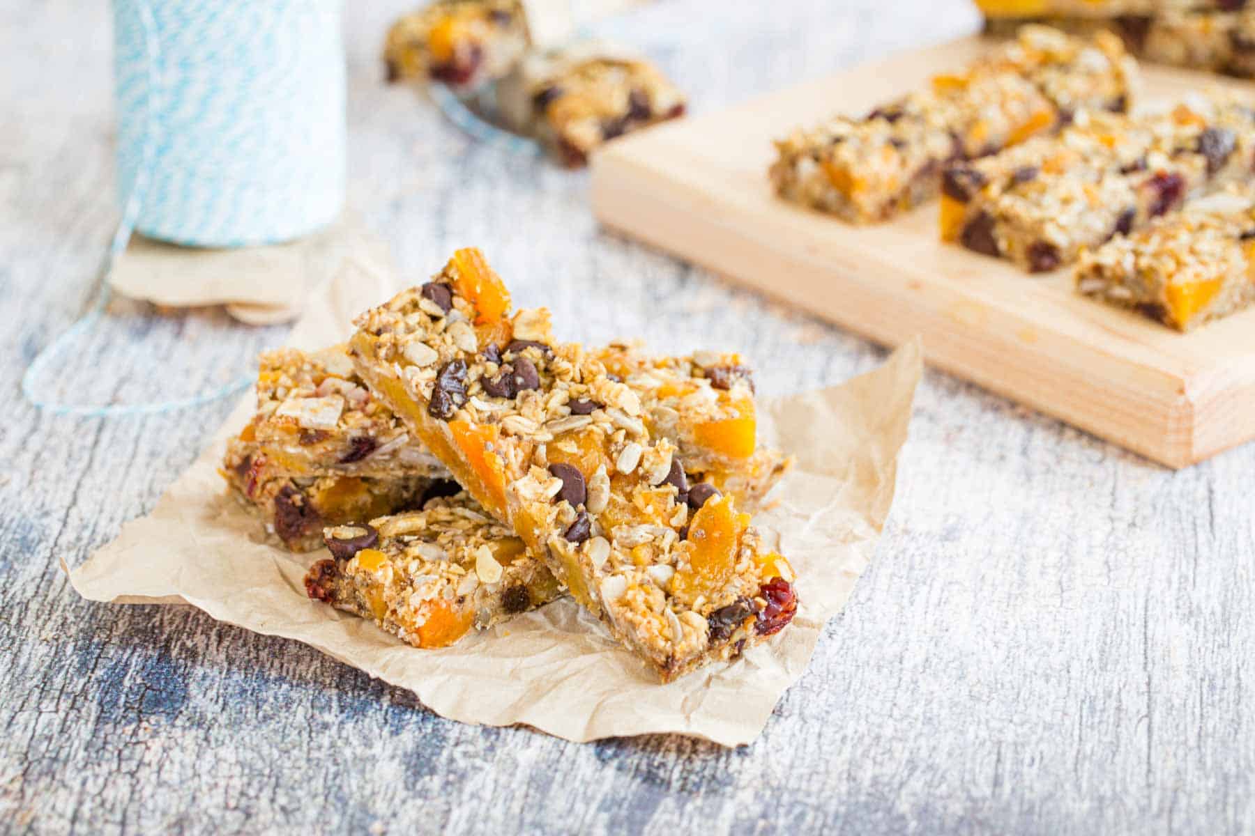 Four Nut-Free Trail Mix Granola Bars on a piece of parchment paper with more behind them on a small cutting board.