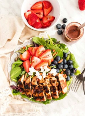 Sliced Grille Chicken Salad topped with berries and goat cheese with a bottle of blueberry balsamic salad dressing