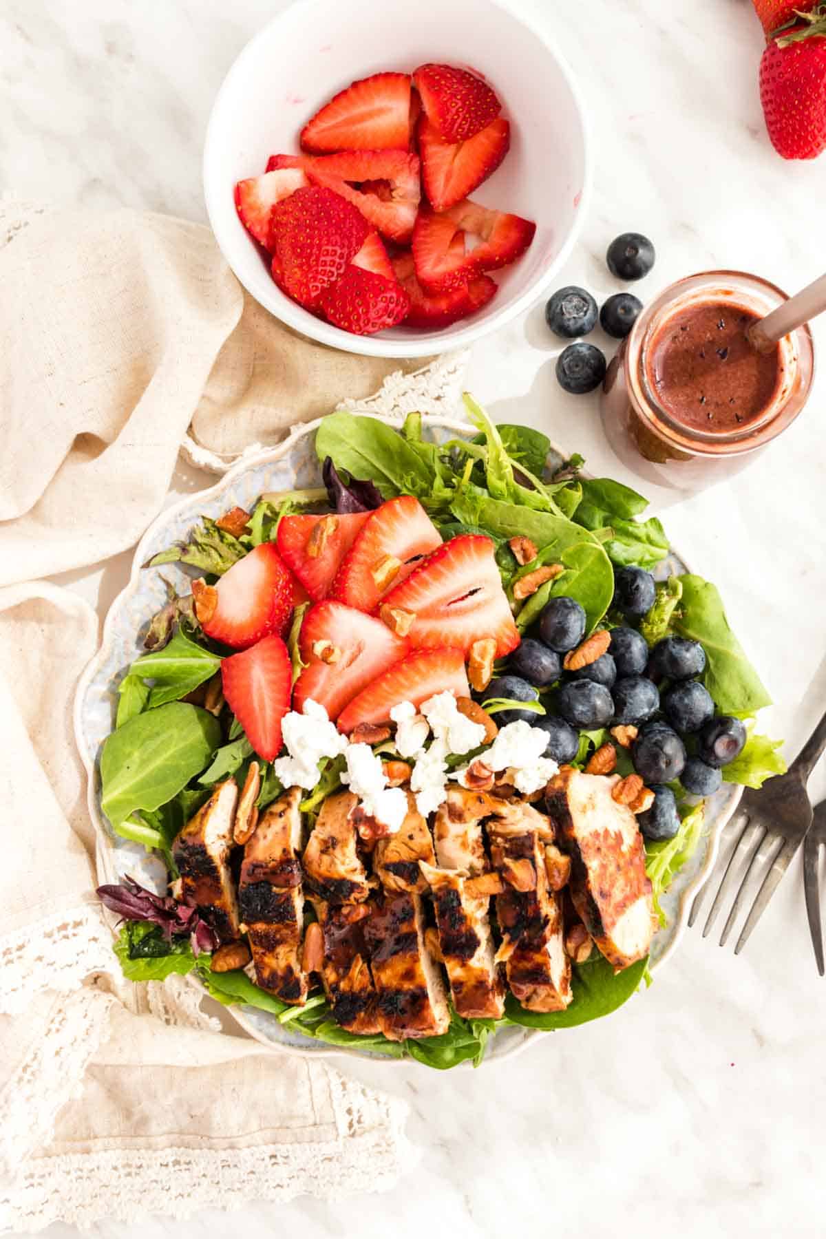 Sliced Grille Chicken Salad topped with berries and goat cheese with a bottle of blueberry balsamic salad dressing