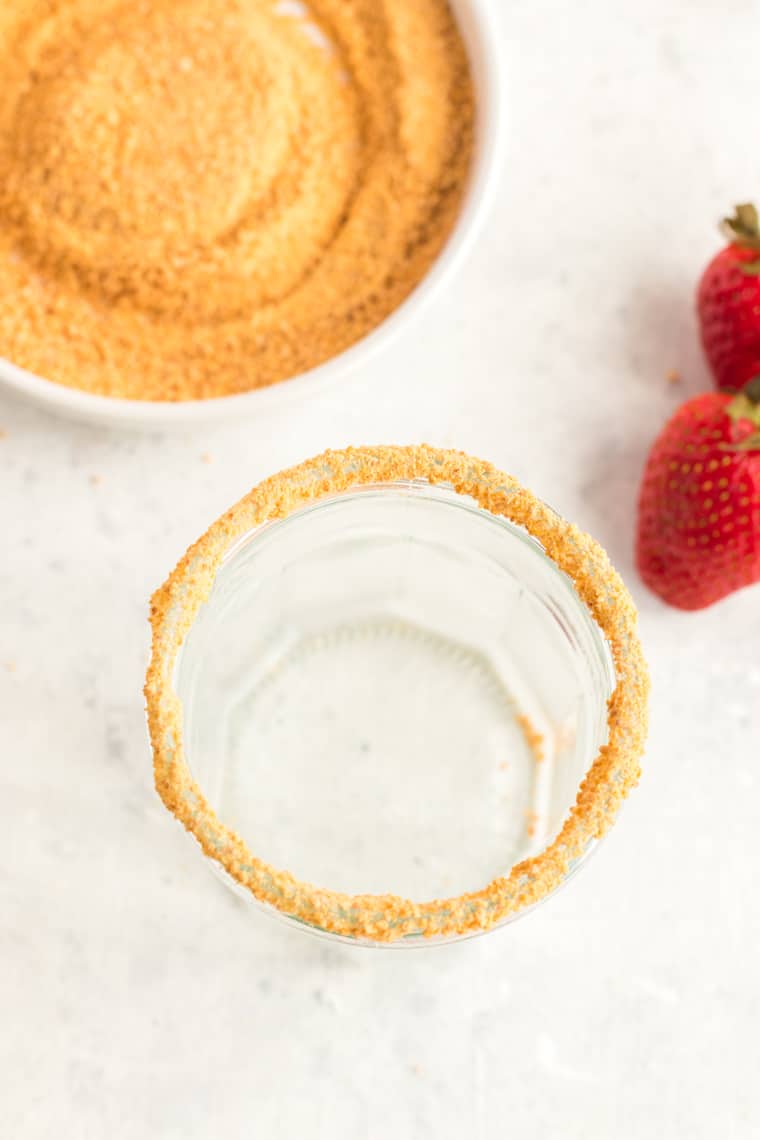 Putting graham cracker crumbs on the rim of a glass for a cheesecake-flavored strawberry smoothie