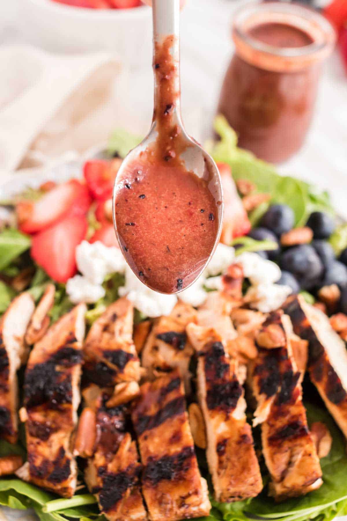 Blueberry Balsamic Dressing dripping off a spoon onto a salad with grilled chicken.