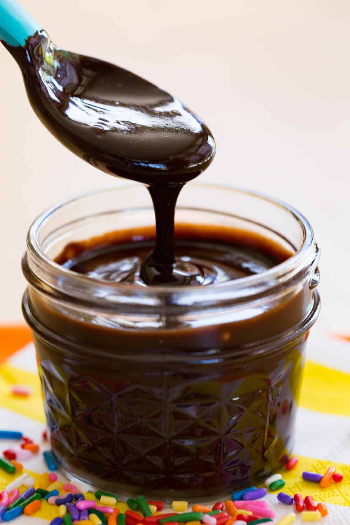 A spoon drizzling hot fudge sauce back into the jar