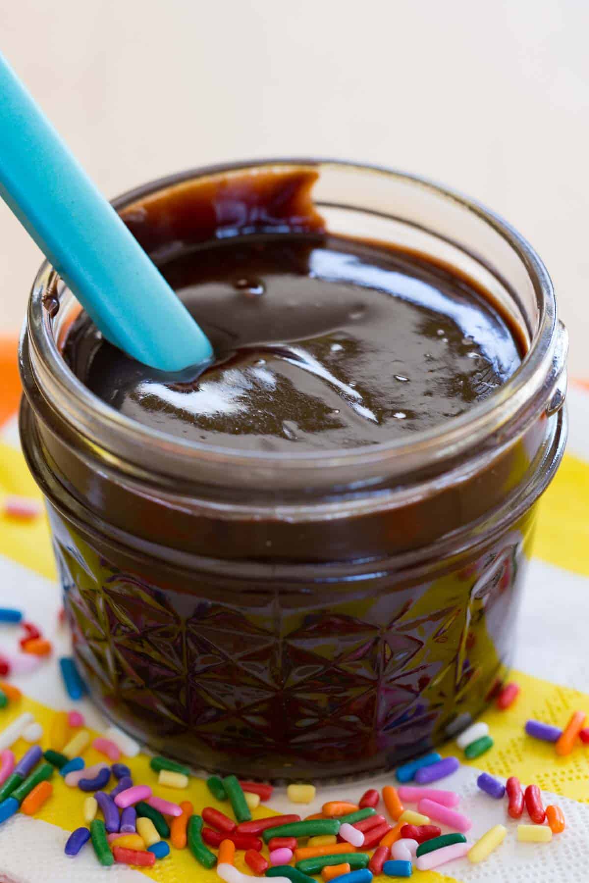 A blue spoon in a glass jar of hot fudge sauce
