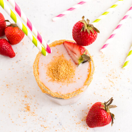 Overhead of a Strawberry Cheesecake Smoothie surrounded by strawberries and striped straws