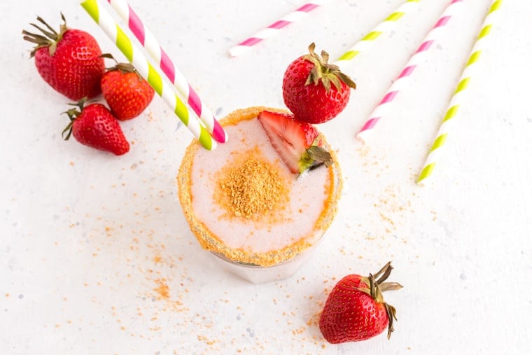 Overhead of a Strawberry Cheesecake Smoothie surrounded by strawberries and striped straws