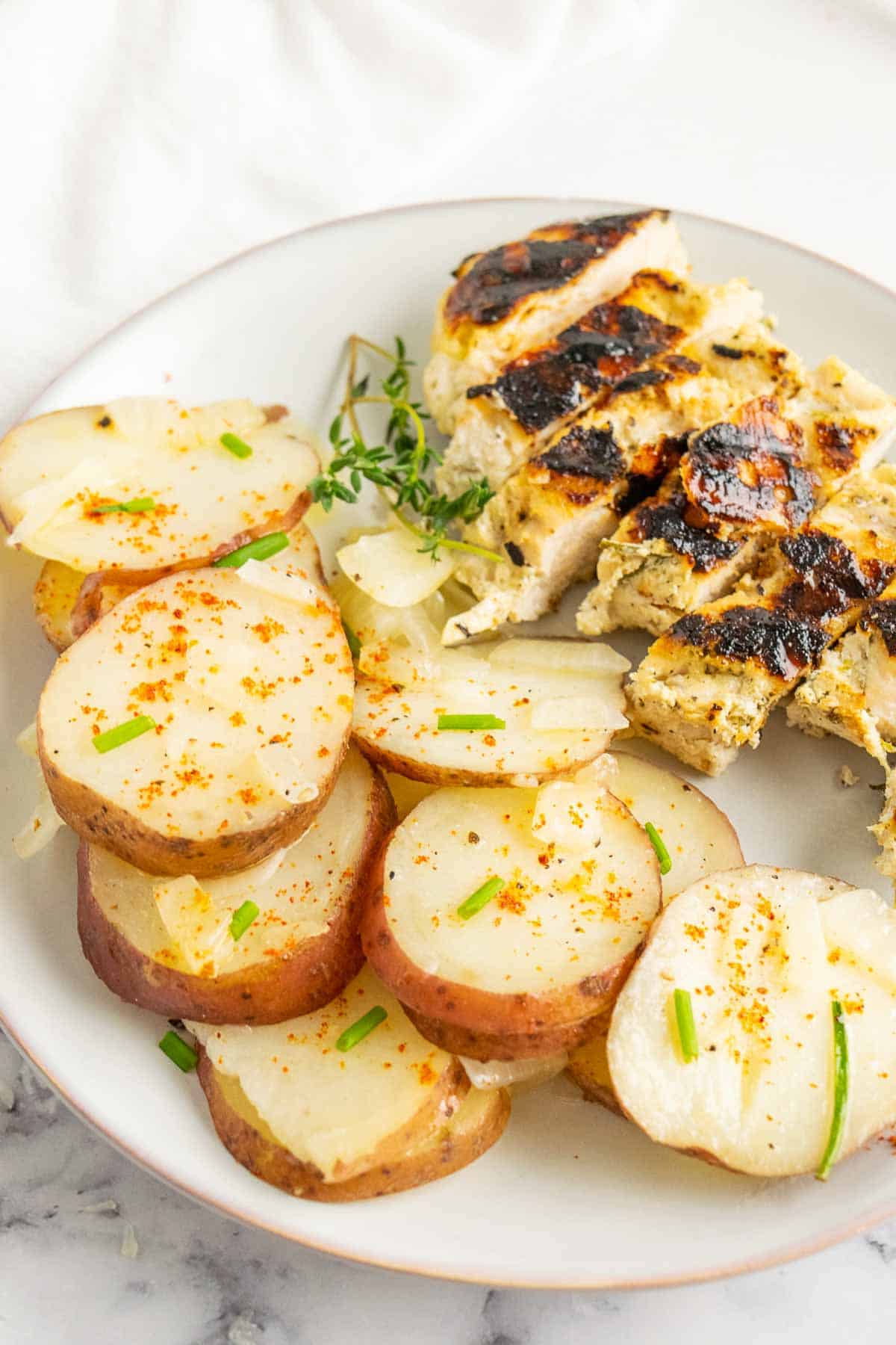 These easy campfire potatoes are smothered with butter and cooked in foil over a fire, on the grill, or in the oven with minimal clean-up! Sliced potatoes served on a plate with grilled chicken.
