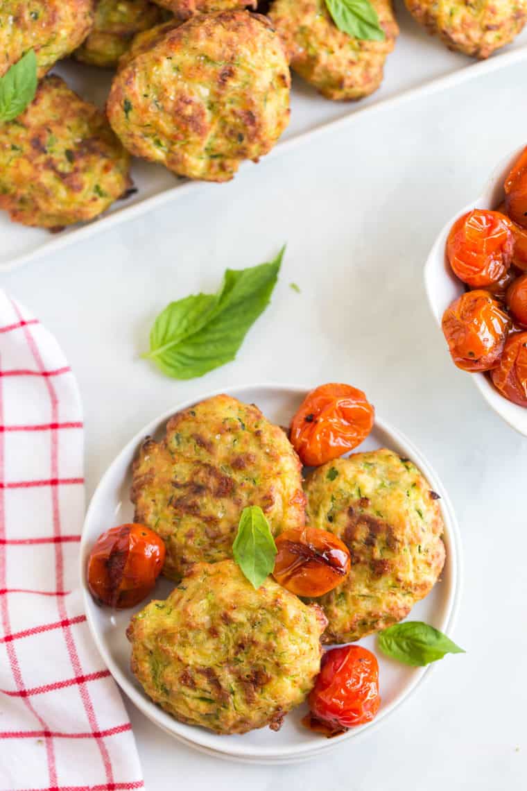 Overhead of three Mozzarella Zucchini Fritters on a small plate topped with balsamic roasted tomatoes