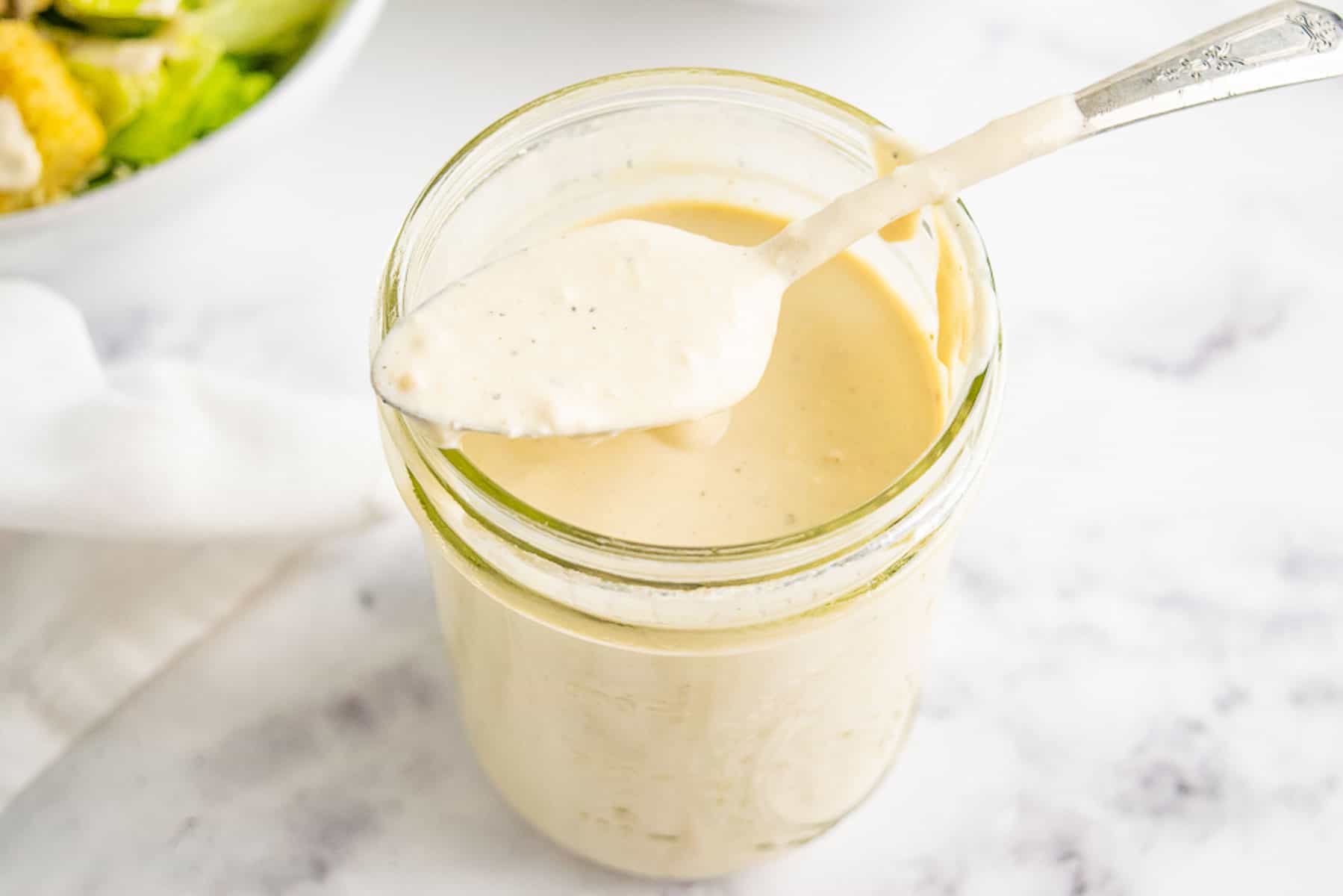 A spoon resting on top of a jar with Greek yogurt Caesar dressing.