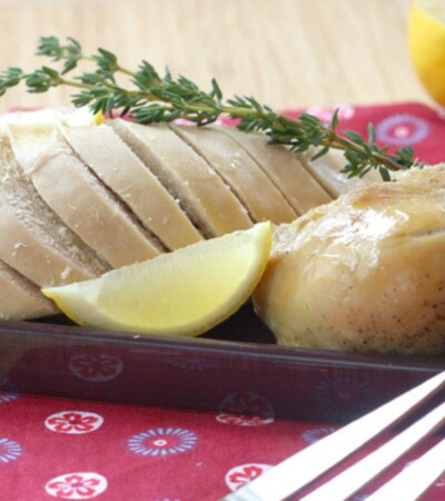 Cut up slow cooker roast chicken on a platter with lemon wedges and a sprig of thyme