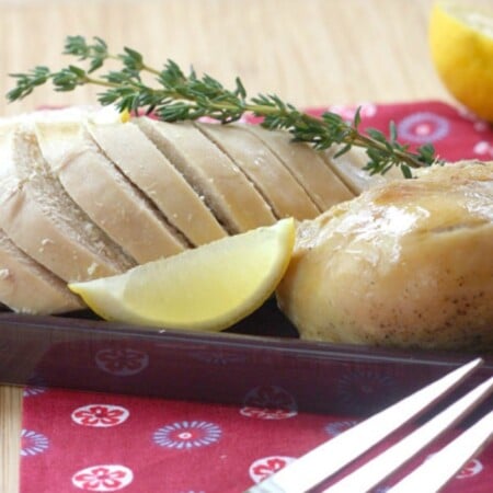 Cut up slow cooker roast chicken on a platter with lemon wedges and a sprig of thyme