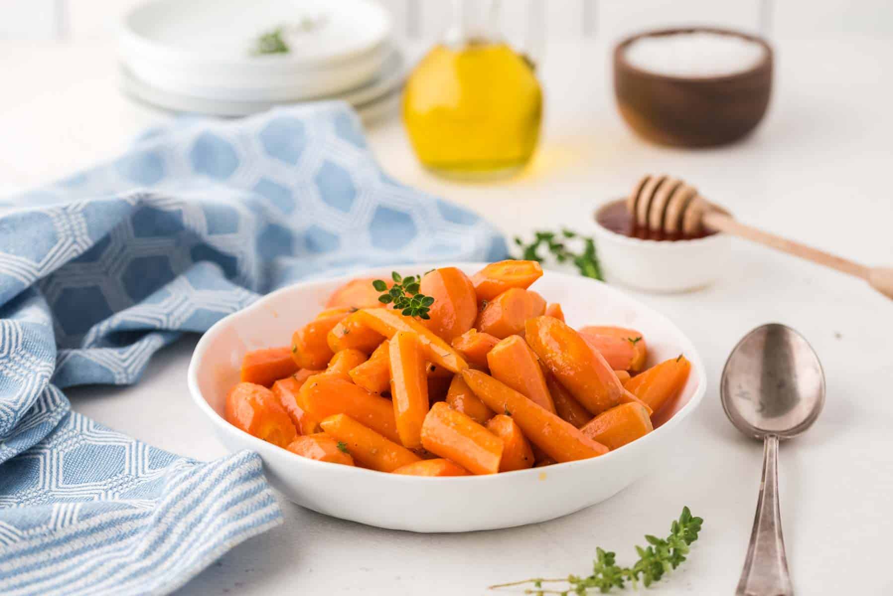 White serving bowl with oven roasted carrots and containers of honey, olive oil, and salt in the background