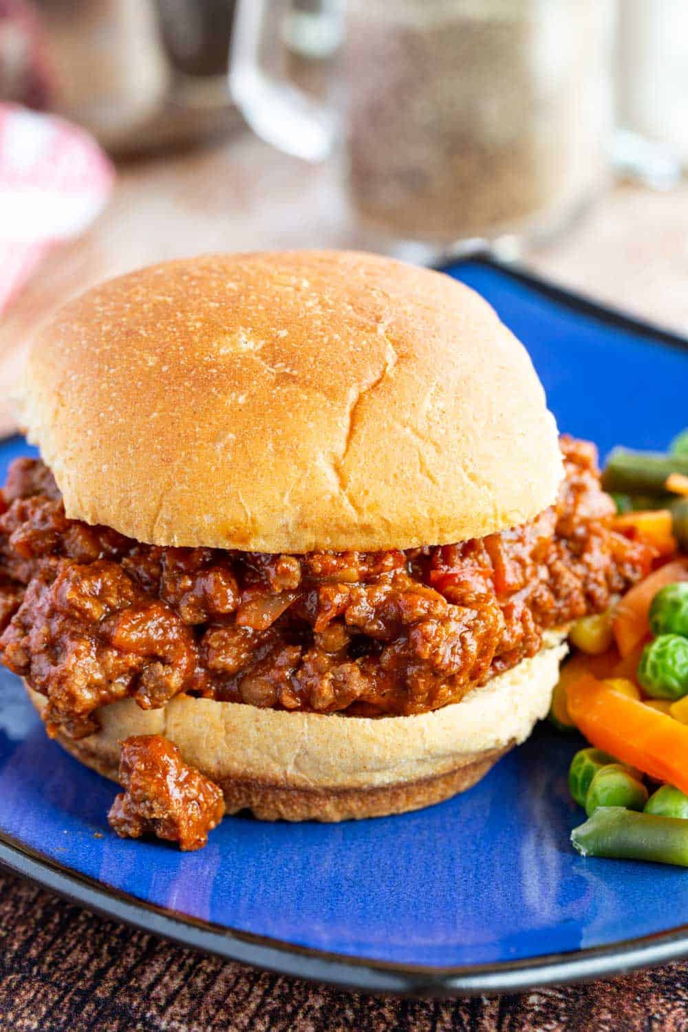 Sloppy joes piled on a bun with mixed veggies on a blue plate.