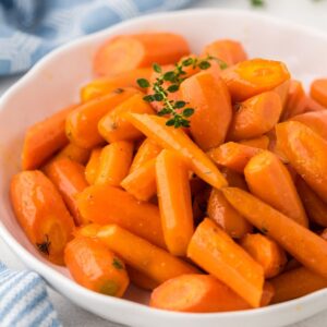 A bowl of honey glazed carrots garnished with a sprig of thyme.